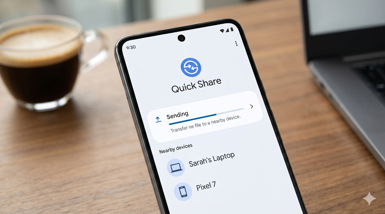 Phone screen showing Quick Share UI with a progress bar and a list of nearby devices such as Sarah's Laptop and Pixel 7 on a wooden desk beside a cup of coffee.