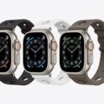 Four smartwatches with square screens and varied band colors (black, white, gray, brown) lined up on a light background.