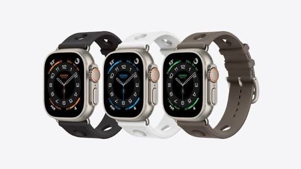 Four smartwatches with square screens and varied band colors (black, white, gray, brown) lined up on a light background.