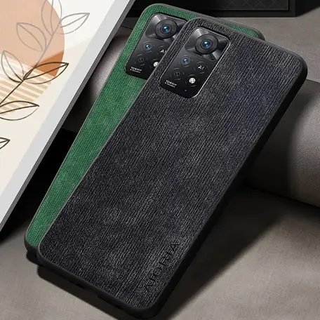 Textured black phone case with a green accent and dual-camera cutout, resting on a couch beside framed art.