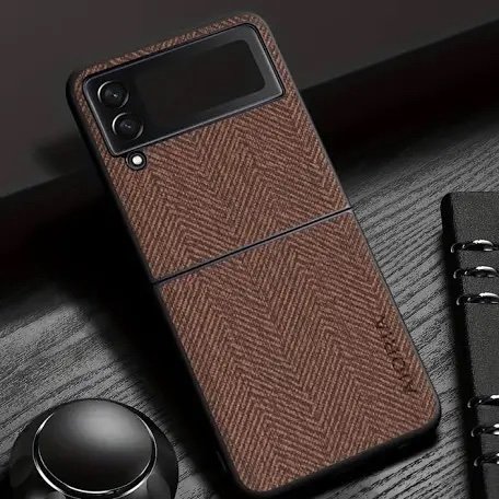 Smartphone with a brown textured leather-looking case on a dark desk, beside a notebook and a round object.