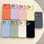 Ten colorful phone cases arranged on a round table in pastel and neutral tones, showing camera cutouts at the top left area of each case.