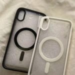 Two translucent iPhone cases with circular ring grip, one black and one white, resting on a soft fabric surface.