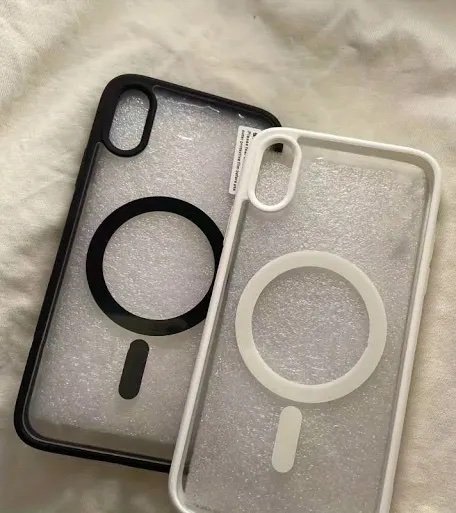 Two translucent iPhone cases with circular ring grip, one black and one white, resting on a soft fabric surface.