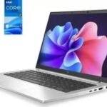 Silver laptop opened at an angle displaying a vibrant wallpaper; floating Intel Core i7 and Windows 11 stickers nearby.